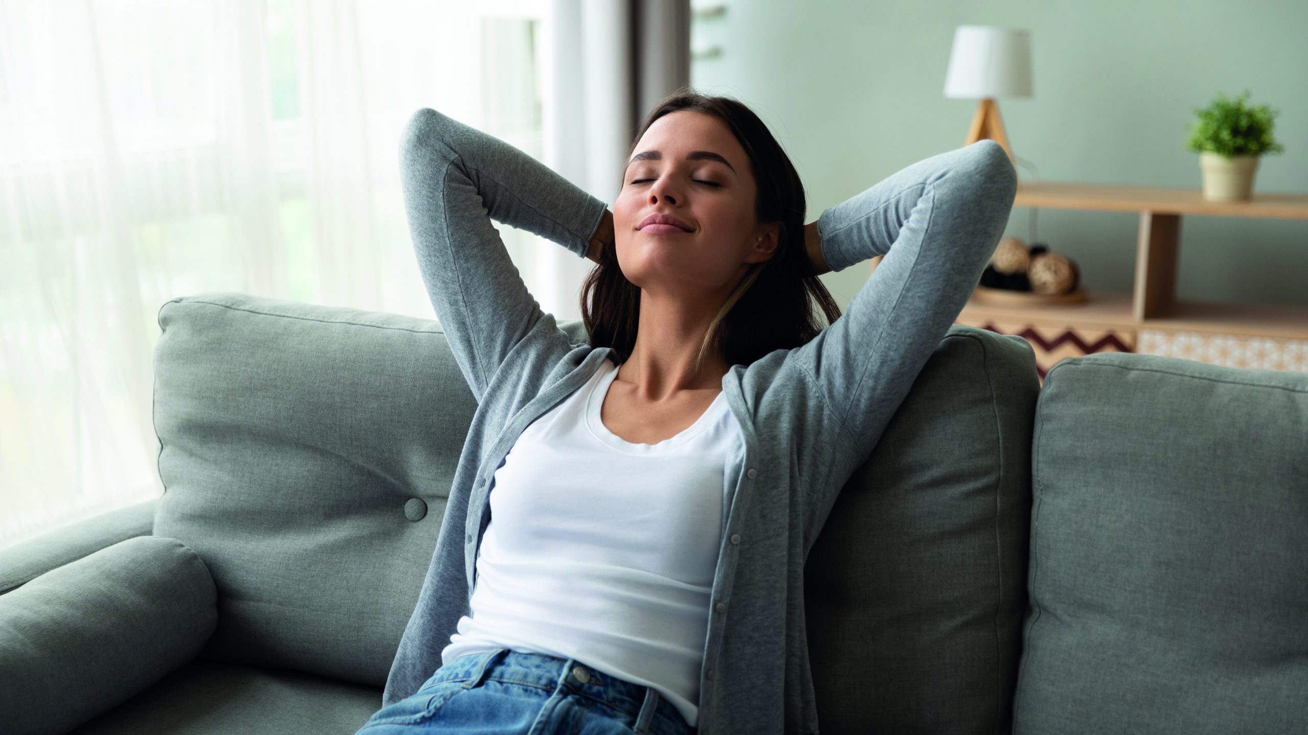 Jeune femme sereine et détendue, allongée sur un confortable canapé à la maison.